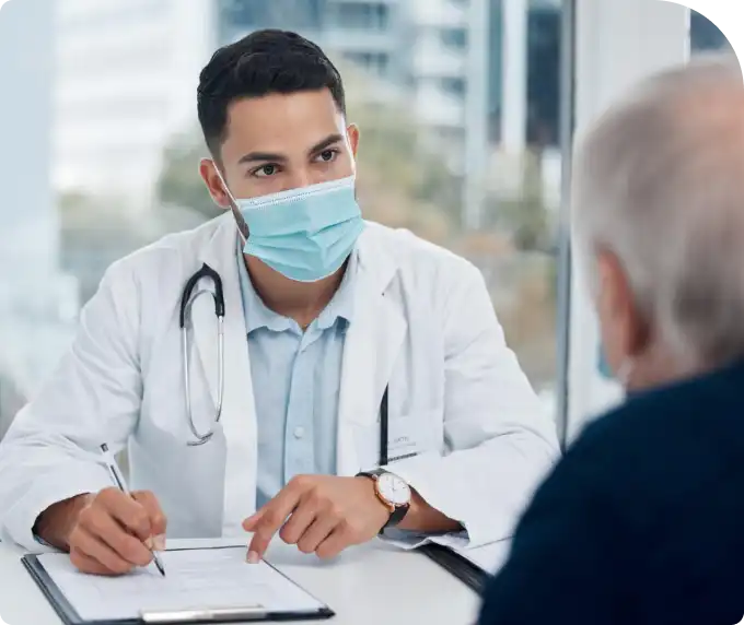 A portrait of a male healthcare professional in a white coat and face mask writing on a clipboard, representing medical professionals in a clinical environment.