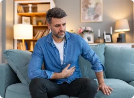 Man sitting on a couch, grimacing in discomfort due to right side abdominal pain.