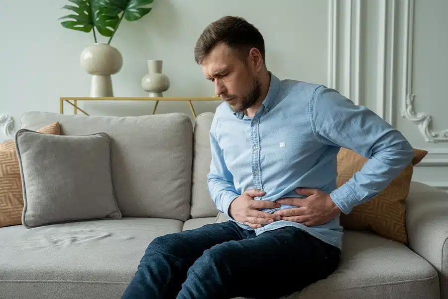 Man experiencing abdominal pain while sitting on a couch.
