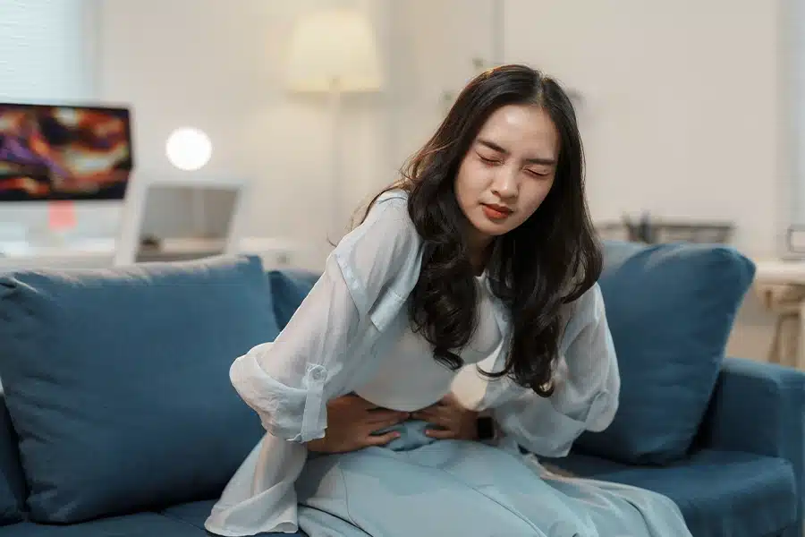 Woman experiencing lower abdominal pain while sitting on a couch.