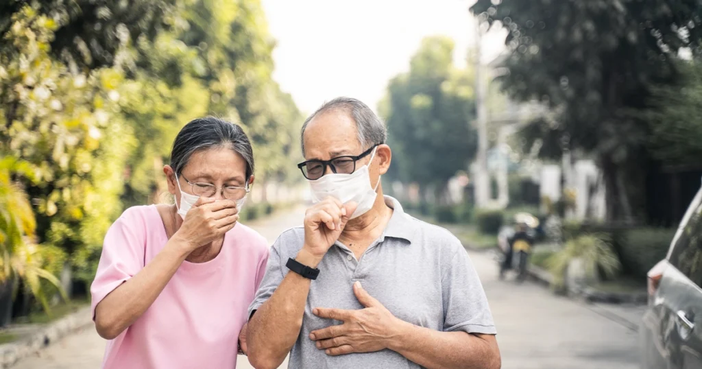 Older couple coughing outdoors while showing pneumonia-like symptoms.