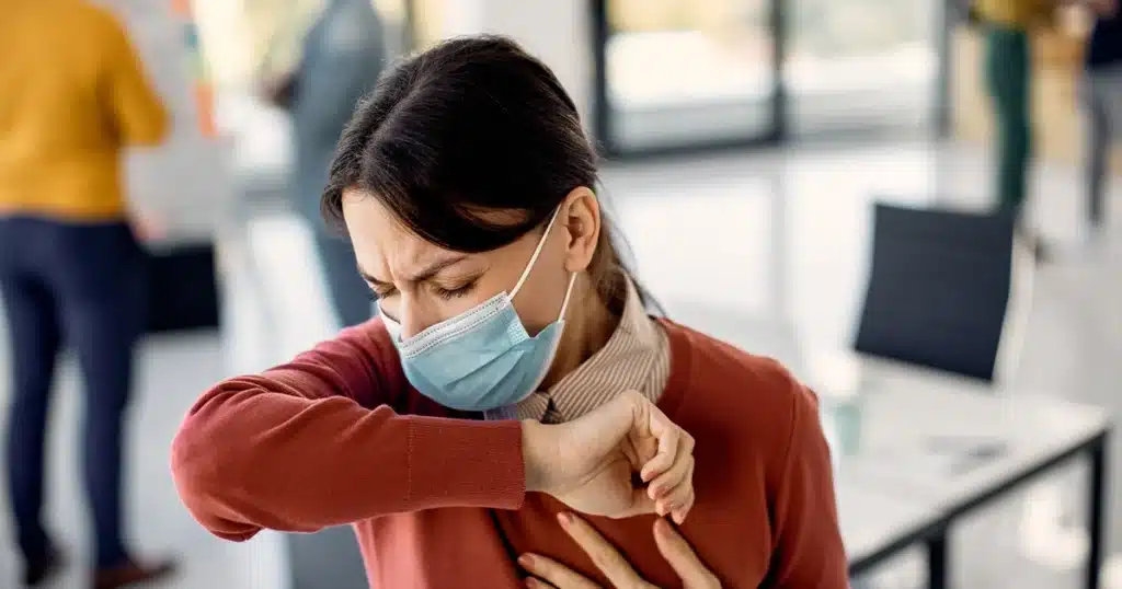 Woman with upper respiratory infection coughing at workplace.