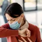 Woman with upper respiratory infection coughing at workplace.