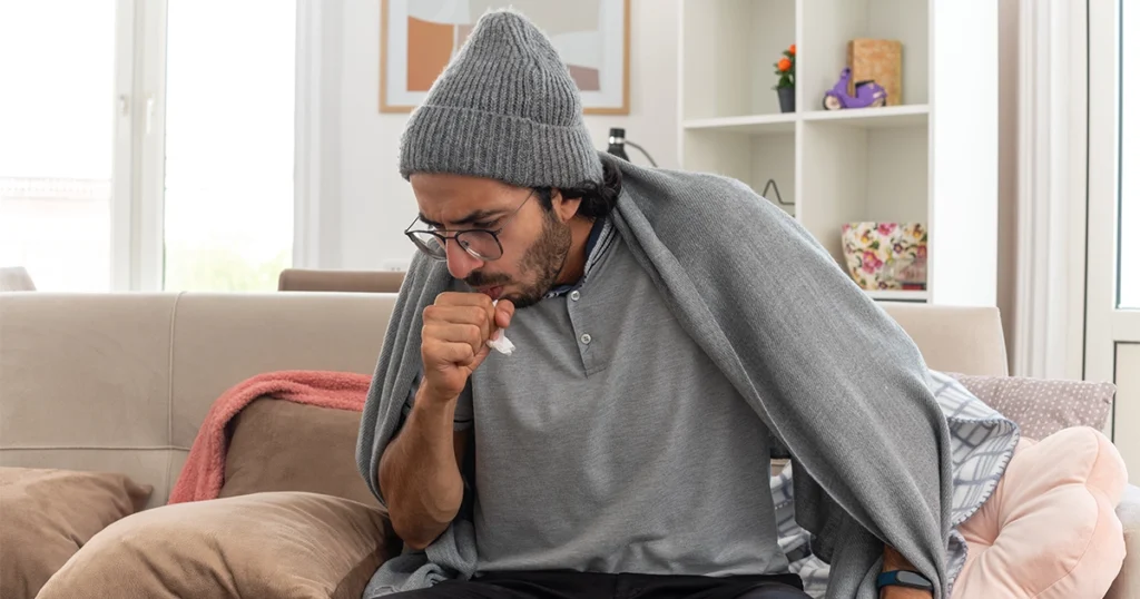Sick man coughing at home while seeking wheezing relief.