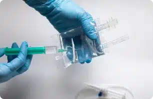 Gloved hands preparing a medical syringe and tubing.