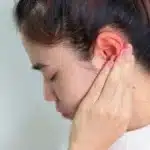 Woman holding painful ear with sore throat symptoms.