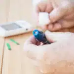 A close-up of a person using a lancing device to perform a blood glucose finger-prick test.