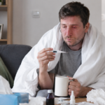 Man with flu symptoms resting at home with tissues and medicine.