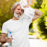 Older man wiping sweat with a towel while holding a water bottle outdoors.