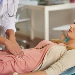 Doctor examining a woman’s lower abdomen during a medical consultation.