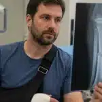 Man with an injured arm in a sling holding an X-ray of a forearm fracture.