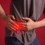 Person clutching their right abdomen with a red glow indicating pain. with a red background.