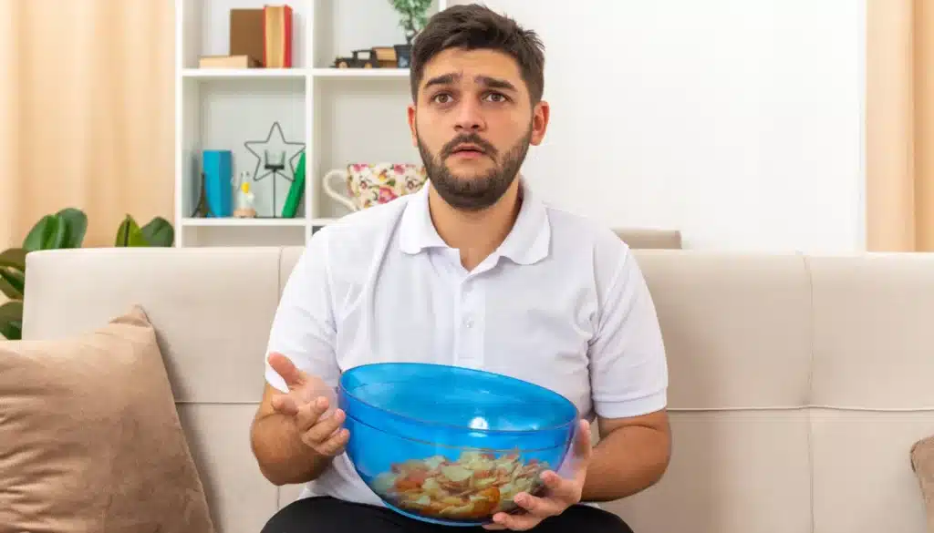 Man sitting on sofa holding a bowl of snack food.
