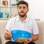 Man sitting on sofa holding a bowl of snack food.