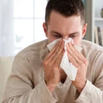Close-up of a sick man holding a paper tissue to his nose, illustrating cold, flu, or seasonal allergy symptoms.