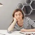 Exhausted woman leaning her head on hand while sitting at desk.