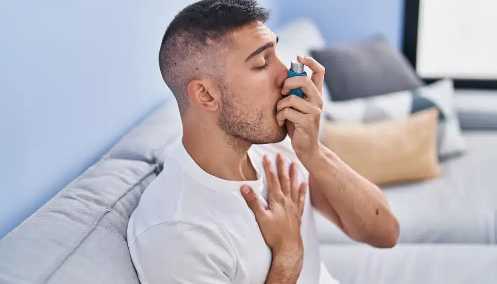 Man on sofa using a blue inhaler for asthma treatment