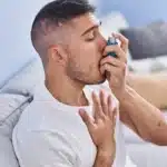Man on sofa using a blue inhaler for asthma treatment