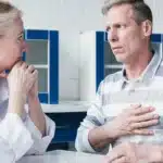 Man touching chest in pain while speaking to a doctor