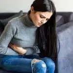 Woman holding her stomach in pain while sitting on couch.