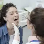 Doctor examining a female patient's throat using a tongue depressor.